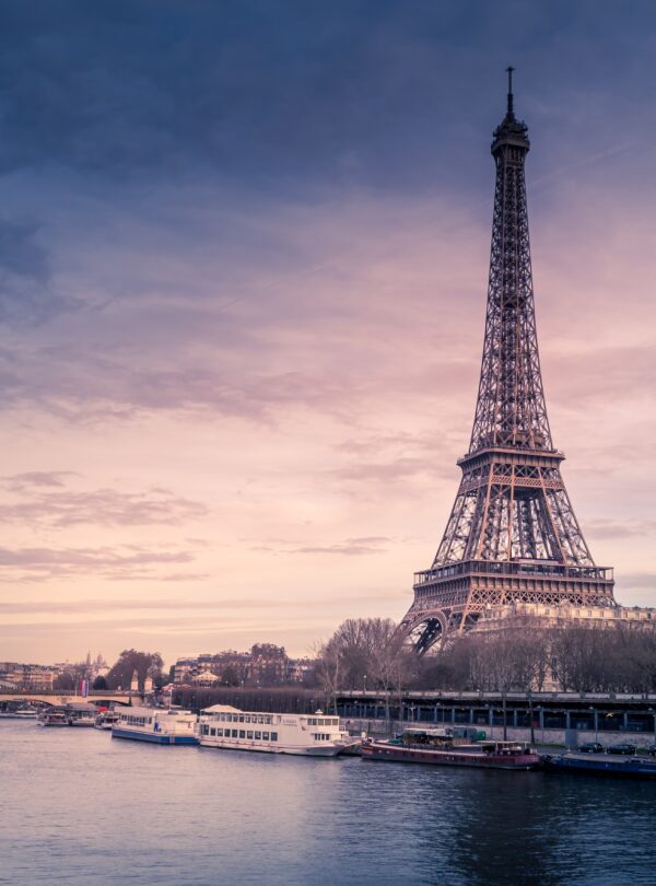 Beautiful wide shot of Eiffel Tower in Paris surrounded by water with ships under the colorful sky